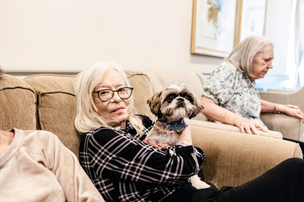 An older adult sitting with a small dog in a community lounge